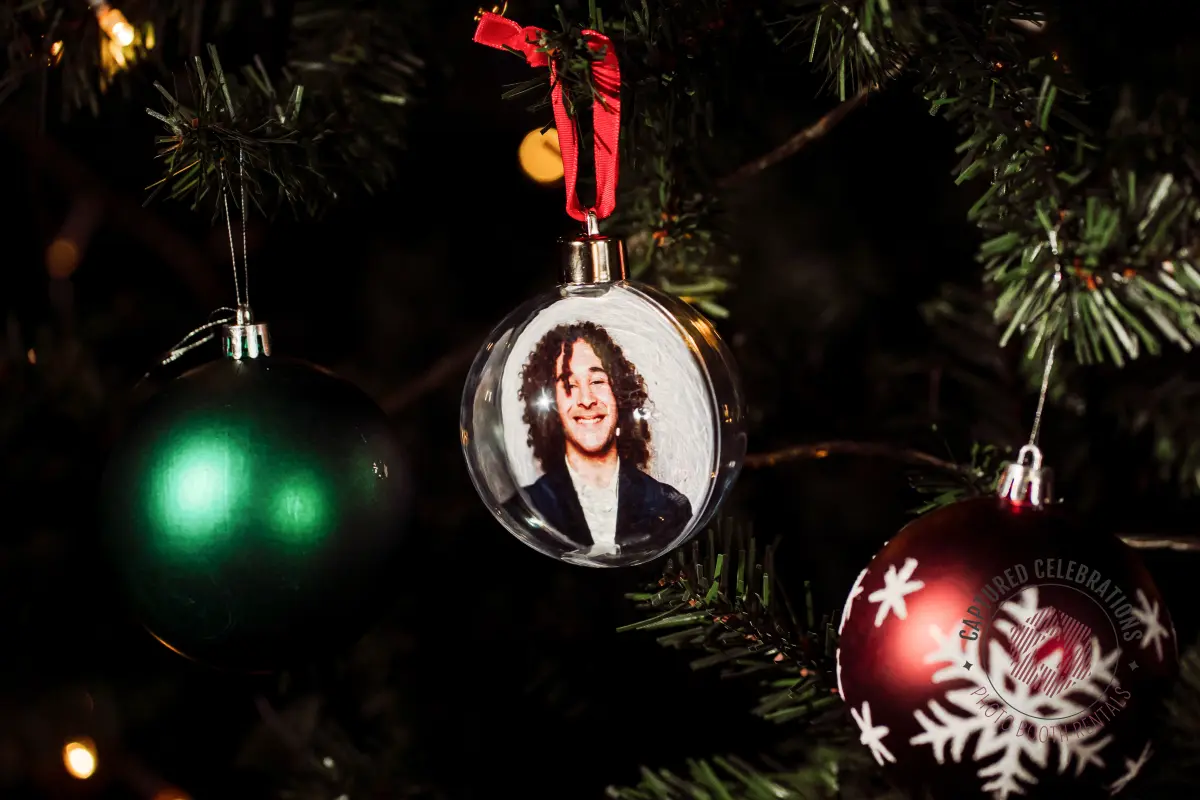 Photo ornament keepsake hanging on a decorated Christmas tree beside traditional ornaments